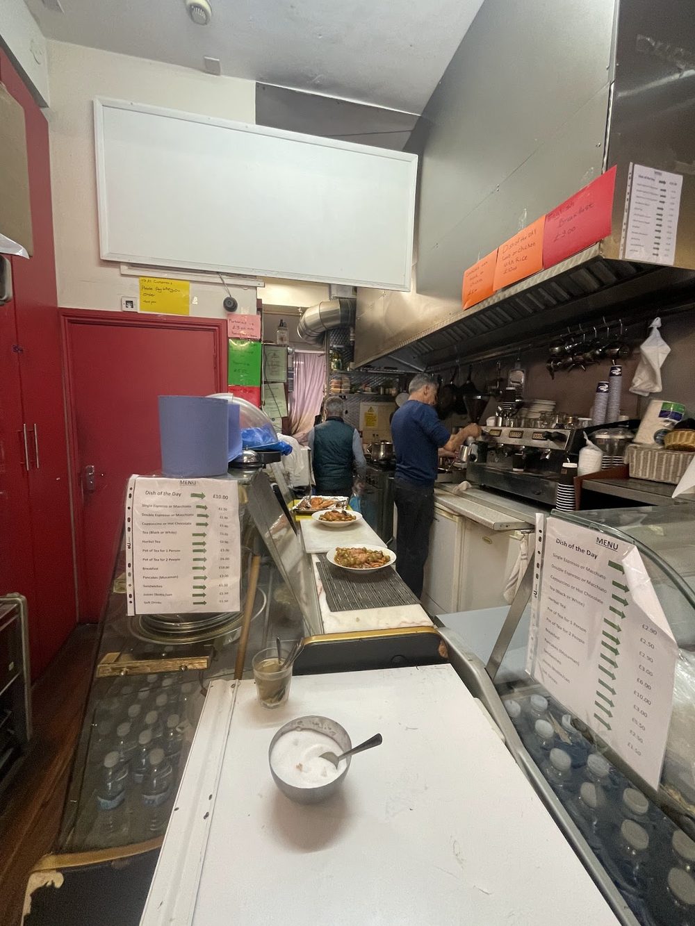 Inside the narrow kitchen and service counter, with the stainless serving line and staff working at the back